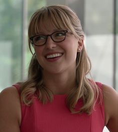 a woman with glasses smiling for the camera in front of a glass wall and window