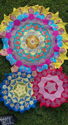 four circular quilts laid out in the grass on top of each other, all different colors