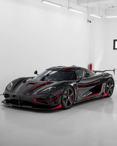 a black and red sports car is parked in a white room with an open door