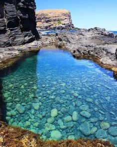 clear blue water surrounded by rocks on the shore with green algae growing in it's bottom