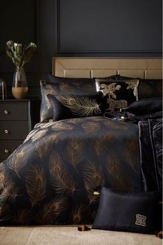 a bed with black and gold comforters in a room next to a vase filled with flowers