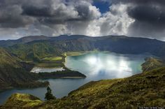 a large body of water surrounded by lush green hills and clouds in the sky above