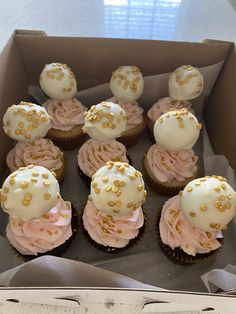 twelve cupcakes with white frosting and gold sprinkles in a box