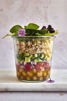 a glass jar filled with salad on top of a white counter next to a purple flower