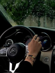 a person driving a car in the rain with their hand on the steering wheel while holding an electronic device