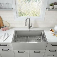 a stainless steel sink in a kitchen with white counter tops and drawers on the side