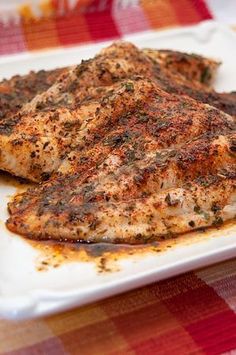 a white plate topped with chicken covered in seasoning on top of a checkered table cloth