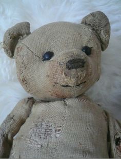 an old teddy bear sitting on top of a white fur covered bedding with eyes wide open