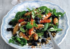 a blue and white plate filled with salad on top of a wooden table next to a fork