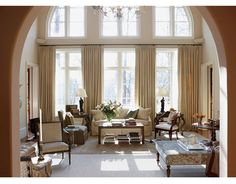 a living room filled with lots of furniture next to large arched windows on the wall