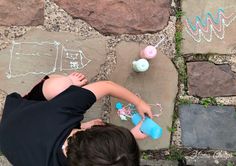 a little boy laying on the ground next to some rocks and chalk drawings with writing on them