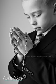 a young boy dressed in a suit and tie holding a rosary with his hands together