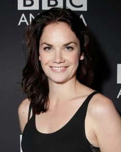 a woman in black tank top smiling at the camera with her hand on her hip