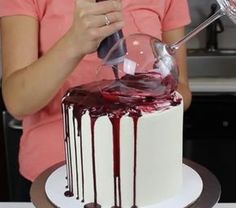 a woman is decorating a white cake with red icing