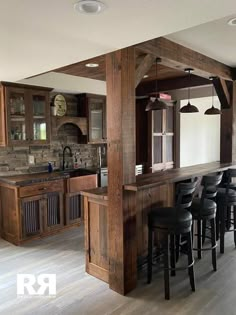 a kitchen with wooden cabinets and black bar stools in front of an open floor plan