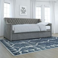 a gray couch sitting on top of a blue rug next to a white bed in a living room