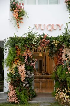 an entrance to a store with flowers and greenery on the outside wall, along with a sign that says yuu