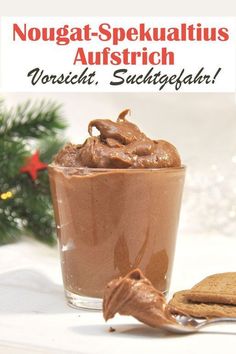 a chocolate dessert in a glass next to a cookie on a table with a christmas tree behind it