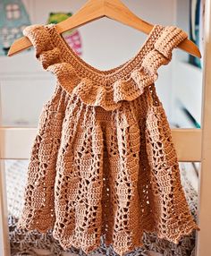 a brown crocheted dress hanging on a wooden hanger in front of a white wall