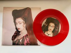 a red record sitting on top of a white table next to a photo of a woman