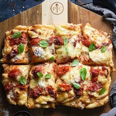 several square slices of pizza on a wooden cutting board with basil leaves and pepperoni