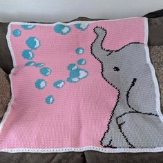 a crocheted blanket with an elephant on it sitting on a couch next to a pillow