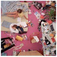 two people sitting on a bed in a cluttered room with pink walls and floor