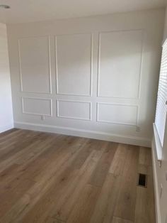 an empty room with white paneling and wood floors