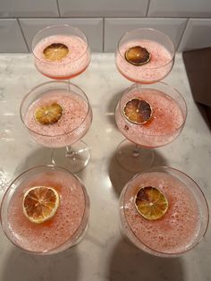 four glasses filled with pink liquid and orange slices on the rims next to each other