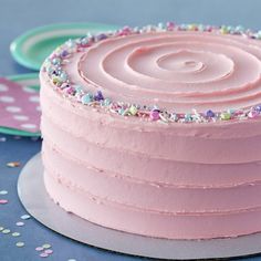 a pink frosted cake with sprinkles sits on a plate next to confetti