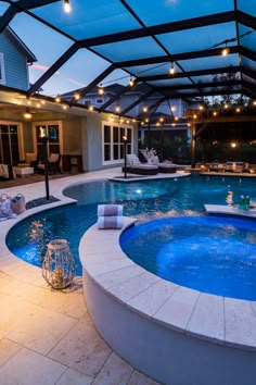 an indoor swimming pool with lights on the ceiling and patio furniture in the back ground