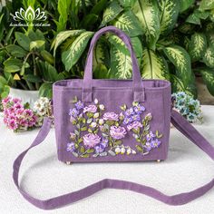 a purple handbag with flowers on it sitting in front of some potted plants