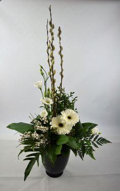 a black vase with white flowers and greenery in it on a gray table cloth