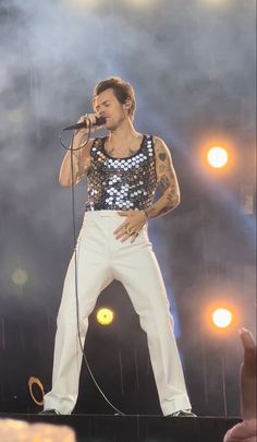 a man in white pants and sequin top singing into a microphone while standing on stage