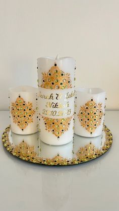 four white candles sitting on top of a plate with gold trimmings and designs