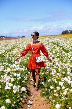 a woman in an orange dress walking through a field of white flowers with her arms outstretched