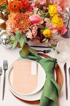 Vibrant table setting with autumn florals including orange chrysanthemums, pink ranunculus, yellow roses, and peach blossoms, complemented by a green linen napkin, white dinnerware, and a peach-colored menu card. Green Table Settings, Floral Tablescape, Autumn Florals, Wedding Furniture, Tablescape Inspiration, Wedding Place Settings, Green Table, Fall Wedding Decorations