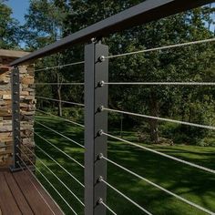 a wooden deck with metal railings next to a stone wall and green grass in the background