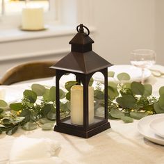 a lit candle sits on a table with greenery and white plates in the background