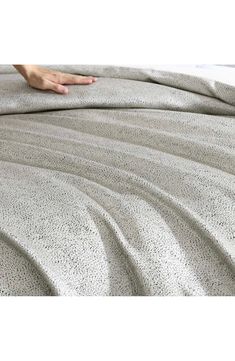 a person's hand is on the edge of a bed with a comforter