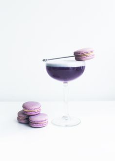 purple macaroons are sitting on the table next to a wine glass and some cookies