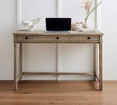 a laptop computer sitting on top of a wooden desk next to a vase with flowers