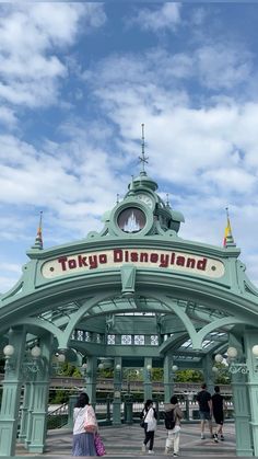 the entrance to tokyo disneyland with people walking under it and onlookers in the background