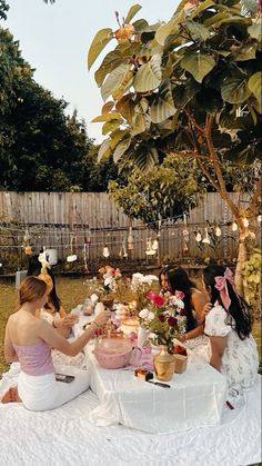 two women sitting at a table with cake and flowers in front of them on the grass