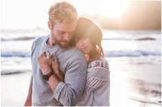 a man and woman embracing each other on the beach at sunset with the ocean in the background