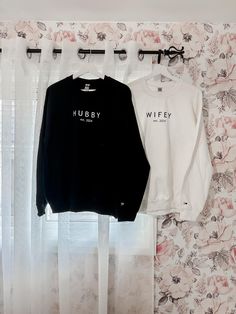 two sweatshirts hanging on the wall in front of a window with floral print curtains