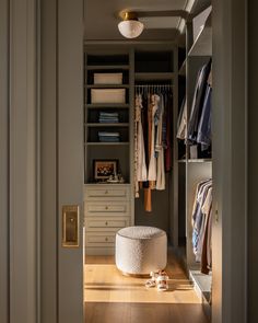 a walk in closet with clothes on hangers and a foot stool next to it