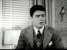 a man wearing a suit and tie sitting in front of a window