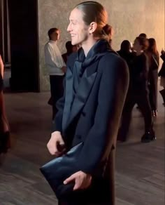 a woman standing in front of a group of people wearing black clothing and holding a blue purse