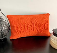 an orange crocheted pillow sitting on top of a table next to a lantern